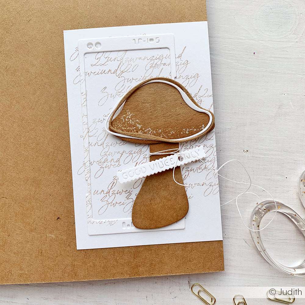 Handgemachte Karte mit einem braunen Pilzausschnitt aus der Alexandra Renke Motivstanze Artist Pilz, einem Gute-Wünsche-Streifen und einem Schrifthintergrund auf hochwertigen weißen Designpapieren.