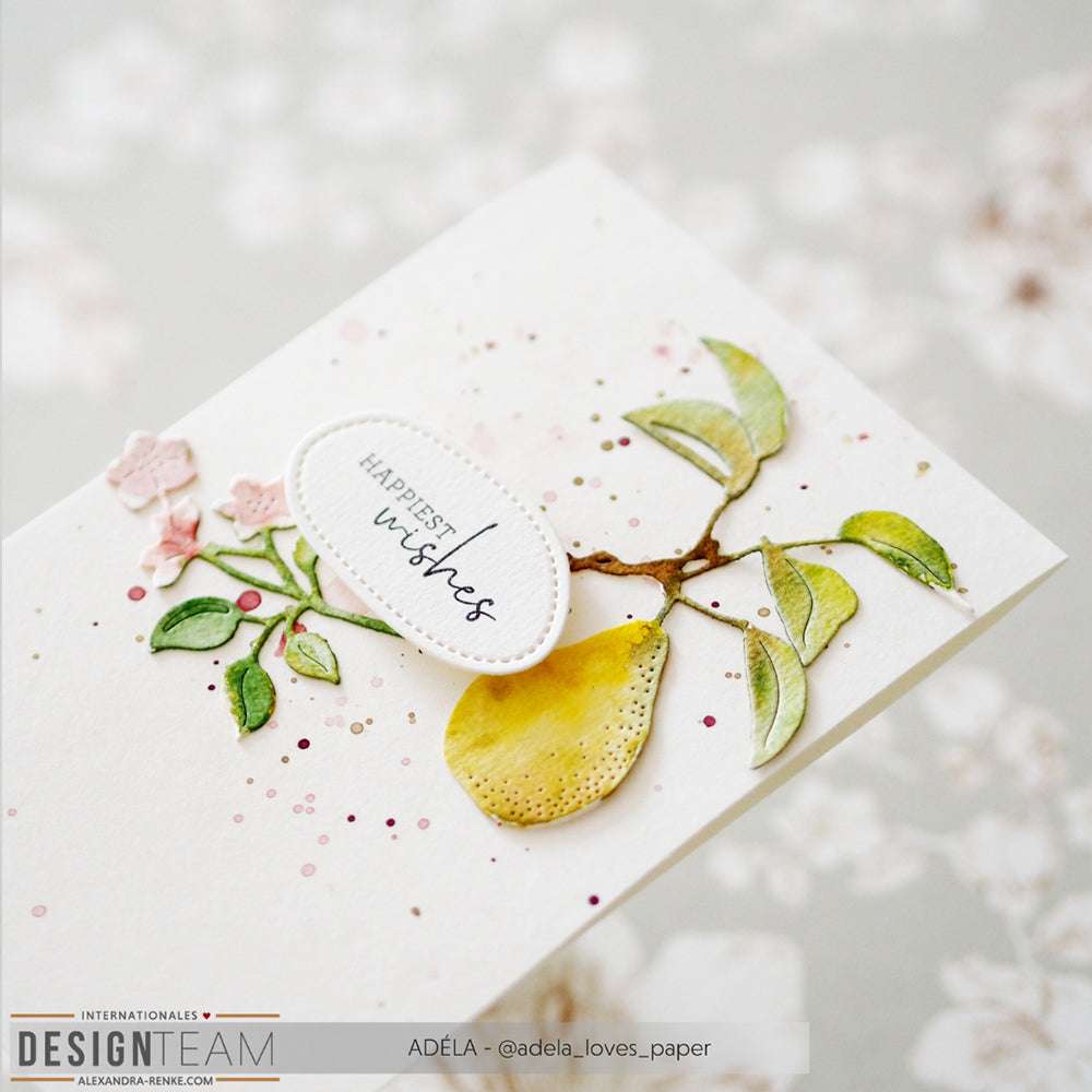 Handgemachte Karte von Alexandra Renke mit einer gelben Birne und Blättern aus Motivstanze Birnenzweig Duo, dem Text "Happiest Wishes" und rosa Farbspritzern auf weißem Designpapier.