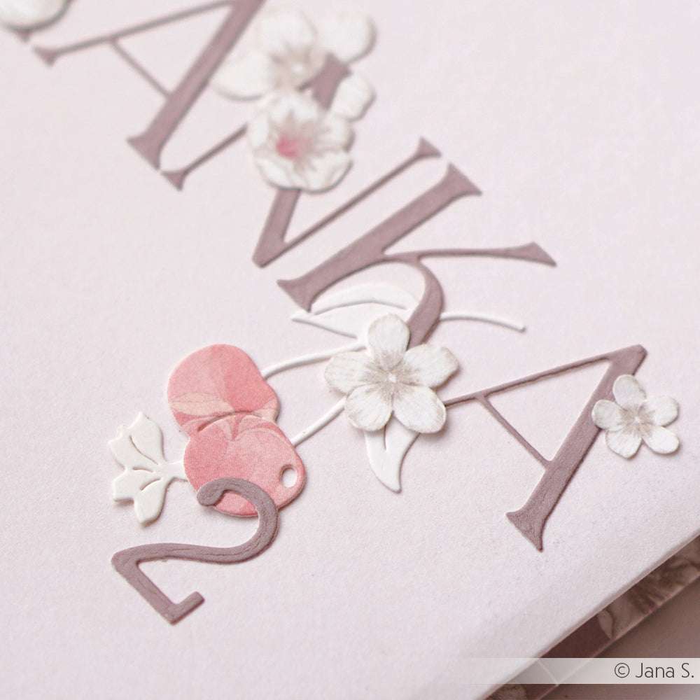 Nahaufnahme eines geprägten Blumen- und Zahlenmusters auf hellem Papier, das "ANKA 2" mit zarten Blumen zeigt - erstellt mit Alexandra Renke DieCut Systemen für präzise Details.