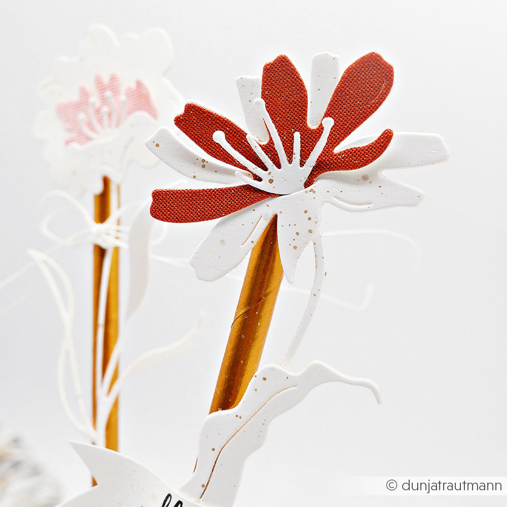 Eine Nahaufnahme einer rot-weißen Schichtblume 8 von Alexandra Renke auf einem braunen Stiel, gefertigt mit Motivstanze, mit einer anderen verschwommenen Blume im Hintergrund.