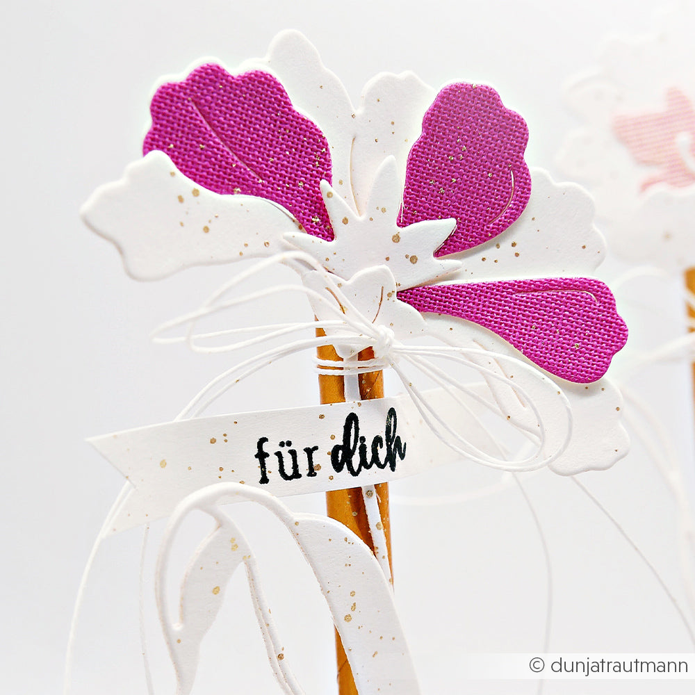 Eine weiße und violette Papierblume mit der Motivstanze Schichtblume 10 von Alexandra Renke und hochwertigen Designpapieren, verziert mit einem "für dich"-Anhänger, auf weißem Hintergrund.