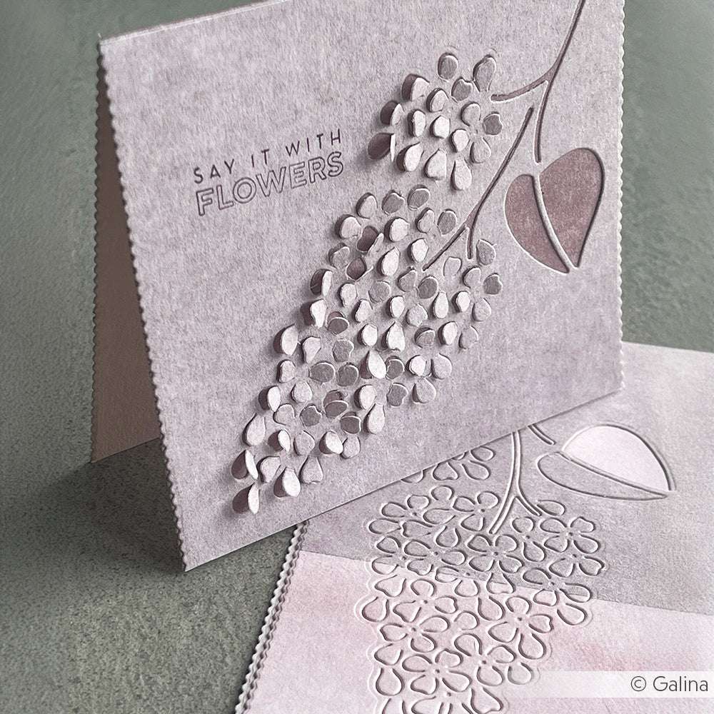 Eine blassviolette Karte von Alexandra Renke mit erhabenen Blumen- und Blattmustern, die mit Stanzsystemen hergestellt wurden, und "SAY IT WITH FLOWERS" auf der Vorderseite.