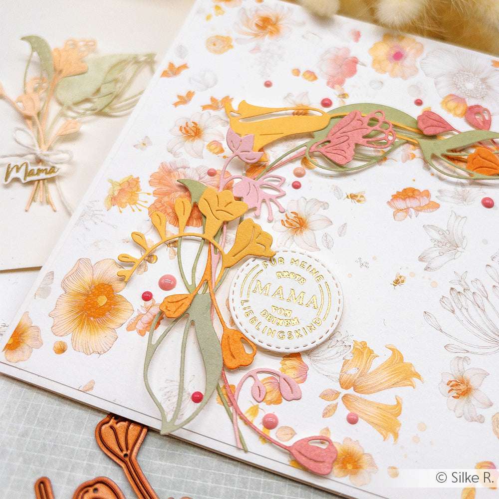 Eine Blumenkarte von Alexandra Renke, die mit der Motivstanze Glockenblümchen aus Designpapier und ausgeschnittenen Blumen gestaltet wurde, mit dem Text "Mama" und pastellfarbenen orange-rosa Verzierungen.