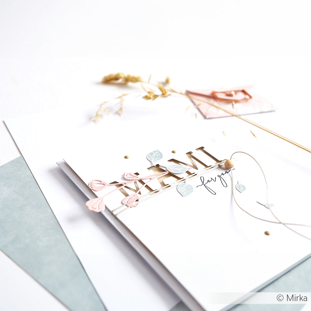 Alexandra Renke Grußkarte mit MAMI in goldenen Buchstaben, floralen Akzenten, getrockneten Blumen und Motivstanzen Wiesenblümchen Trio Details, gestaltet auf weißem Hintergrund.