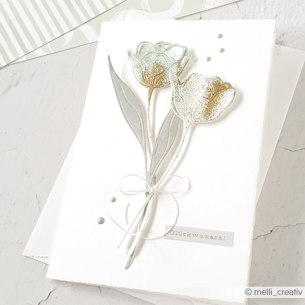Weiße Grußkarte von Alexandra Renke mit zwei geprägten Tulpen aus der Motivstanze Lineart Kelchblume, einer Schleife aus Garn und "Glückwunsch!" auf der Vorderseite.