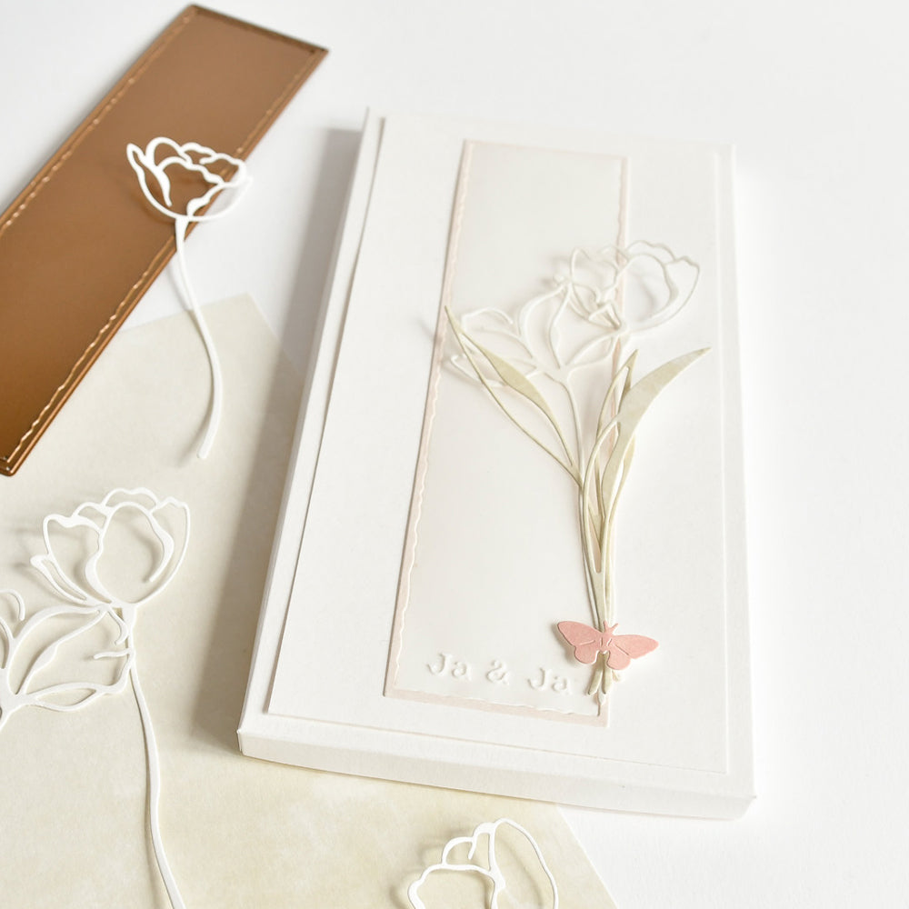 Weiße Grußkarte von Alexandra Renke mit geprägten Tulpen und einem rosafarbenen Schmetterling, gepaart mit Tulpenausschnitten aus Designpapieren, die mit der Motivstanze Lineart Blattwerk gestaltet wurden, sowie einem braunen Lesezeichen.