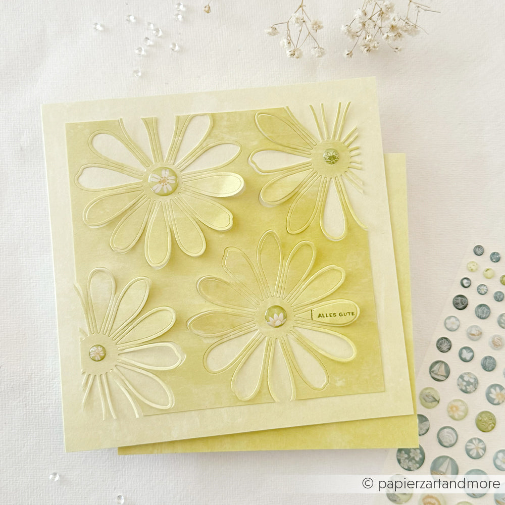 Quadratische gelbe Grußkarte von Alexandra Renke, gefertigt aus Designpapier, mit geprägten Gänseblümchen, die mit der Stanze „Margerite Outline“ ausgestanzt wurden, sowie einem kleinen „Alles Gute“-Schriftzug und dekorativen Akzenten.
