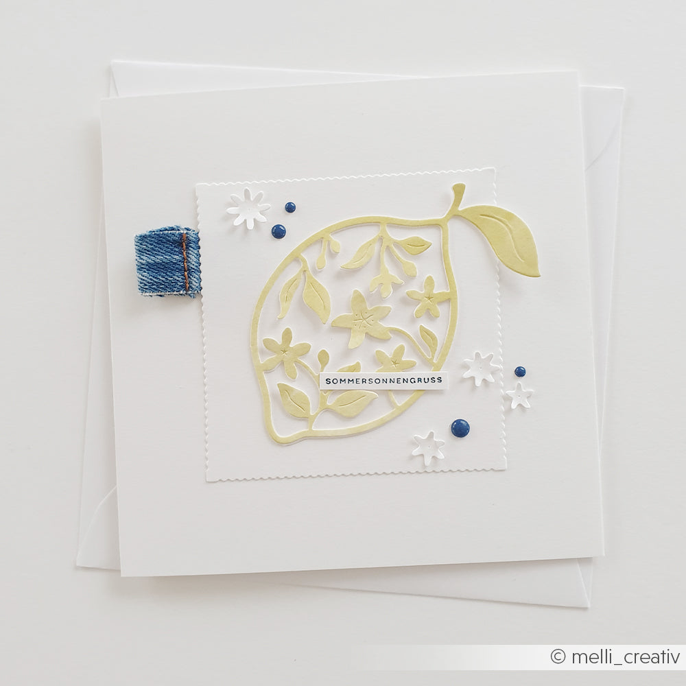 Handgefertigte Karte aus Designpapier von Alexandra Renke mit einem gelben Blatt, zarten weißen Blüten, die mit der Motivstanze „Blumige Zitone“ ausgestanzt wurden, blauen Punkten, einer Verzierung aus Jeansstoff und dem Schriftzug „SOMMERSONNENGRUSS“.