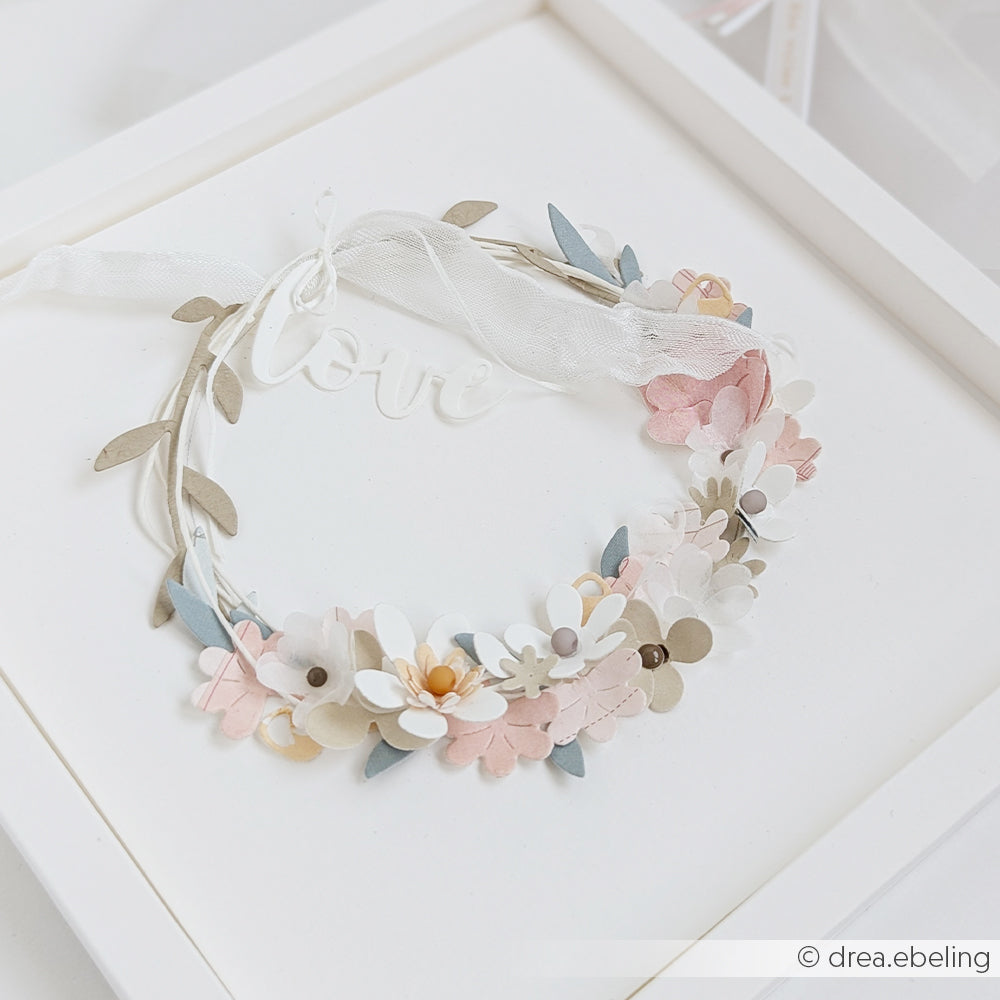 Zarter Blumenkranz aus pastellfarbenen Papierblumen, gefertigt aus Designpapieren von Alexandra Renke und mit der Motivstanze „Streublümchen“, ergänzt durch ein „Love“-Schild, präsentiert in einem weißen Rahmen.