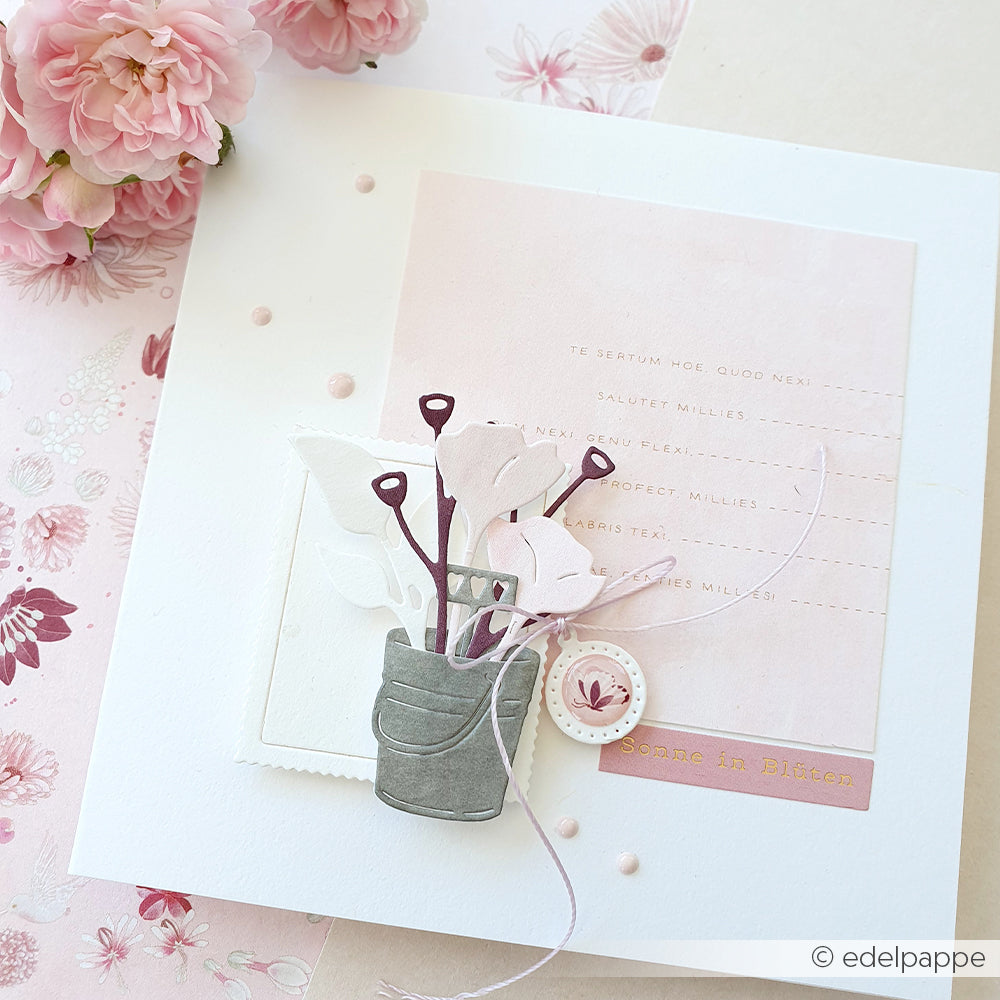 Eine pastellrosa Grußkarte mit Papierblumen, zarten Verzierungen und Akzenten, die mit den Stanzformen „Motivstanze Gartengrüße“ von Alexandra Renke gestaltet wurden und von rosa Blumen umrahmt sind.