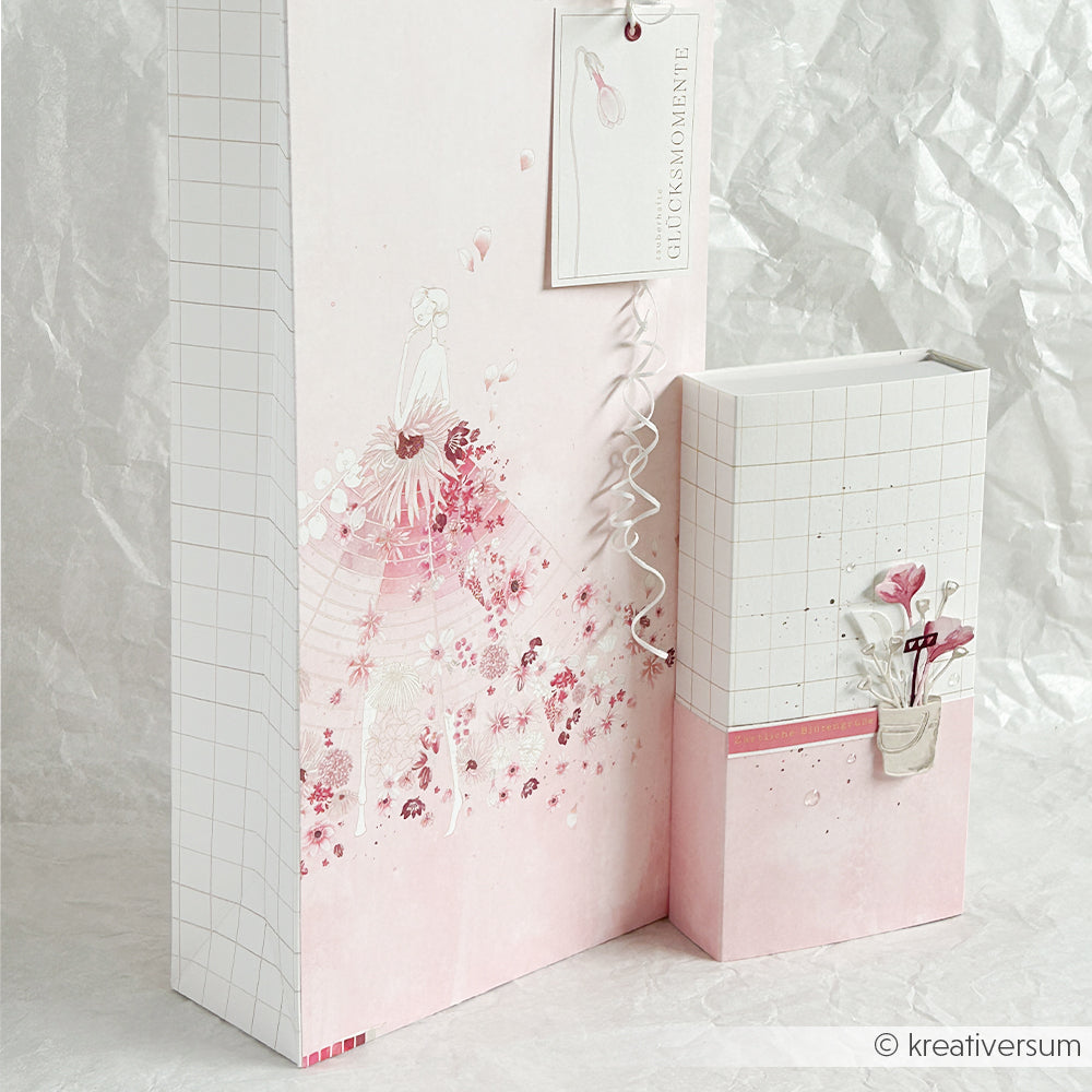 Elegante Geschenkverpackung in Rosa und Weiß mit Blumen- und Gittermustern, verziert mit dekorativen Anhängern und Bändern, die aus Designpapieren von Alexandra Renke und mit der Motivstanze „Gartenfreude“ von Stanzsysteme hergestellt wurden.