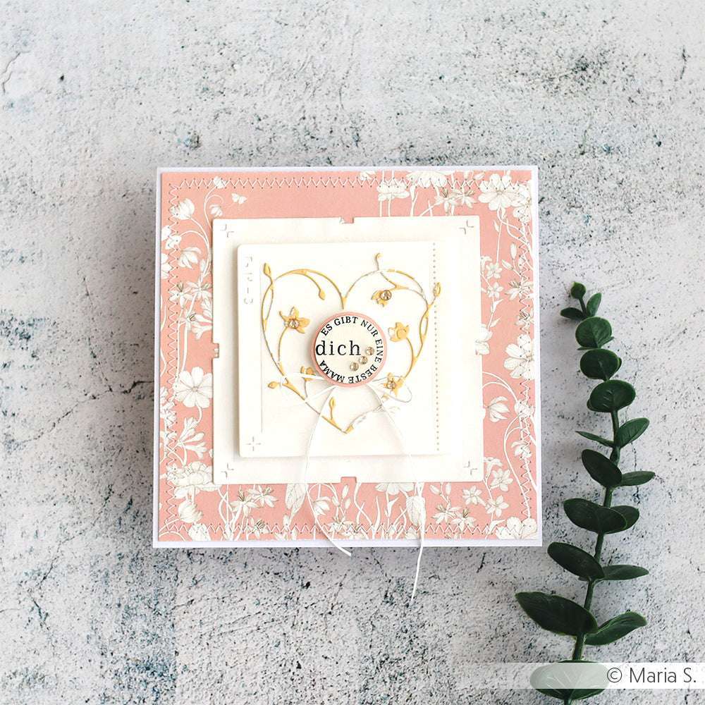 Quadratische Blumengrußkarte auf einer strukturierten Oberfläche mit einem grünen Zweig auf der rechten Seite, hergestellt mit Alexandra Renke Motivstanzen und der eleganten Stanze Florales Herz.