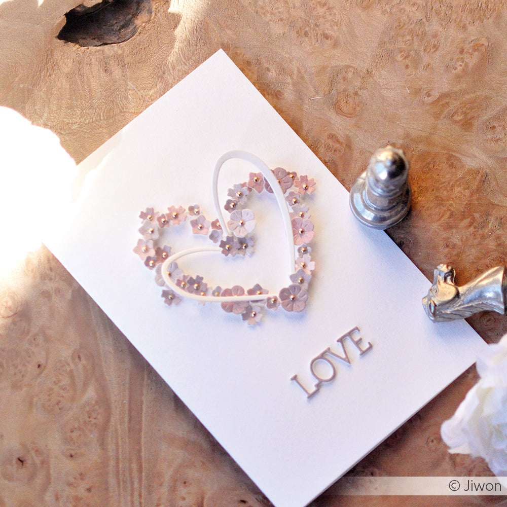 Handgemachte Karte von Alexandra Renke mit einem Herz aus Designpapier, rosa Blumen und dem Wort LOVE neben silbernen Schachfiguren auf Holz.