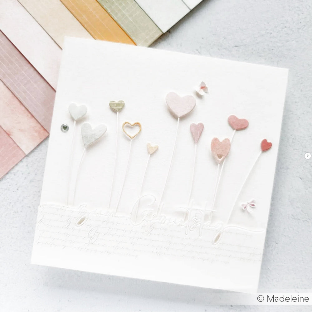 Handgefertigte Karte mit pastellfarbenen Herzformen, erstellt mit Alexandra Renke DieCut Systeme "Motivstanze Herzchen am Stiel", mit kursivem Text und weichen farbigen Papierstreifen im Hintergrund.