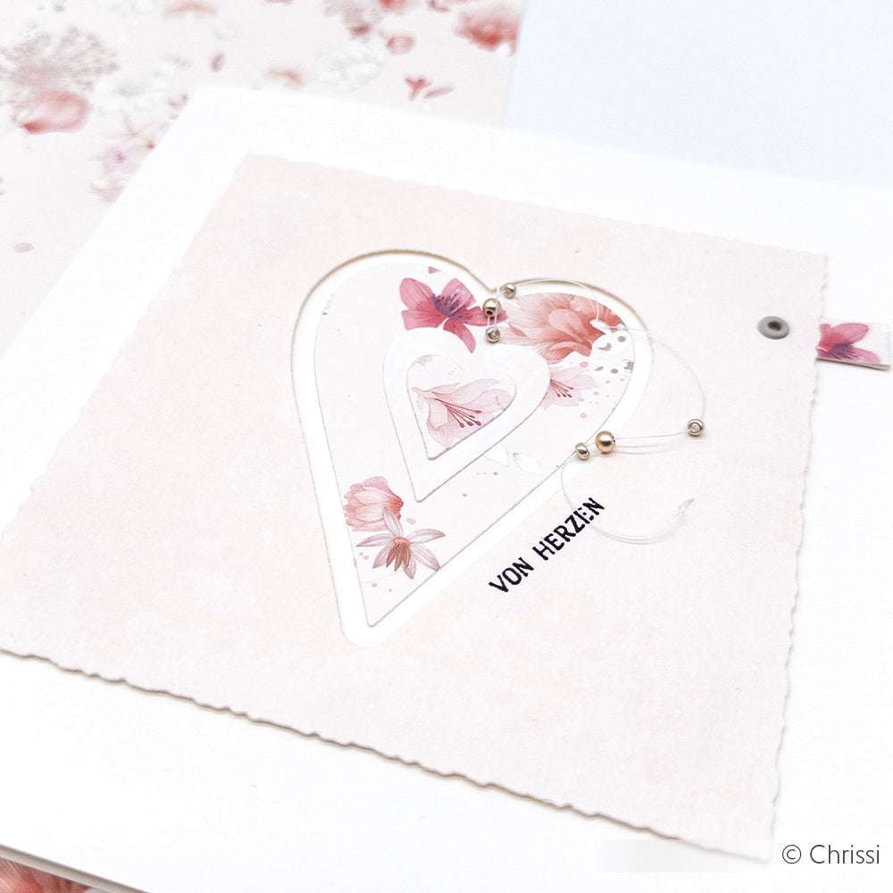 Eine zarte Karte von Alexandra Renke mit floralen Herzausschnitten, rosafarbenen Blumen und dem Text VON HERZEN auf einem zartrosa Hintergrund - perfekt umgesetzt mit Stanzen für Designpapier für präzise, charmante Details.