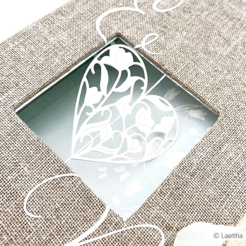 Ein zartes weißes Papierherz mit einer Alexandra Renke Motivstanze ziert eine strukturierte beige Karte mit einem quadratischen Fensterausschnitt.