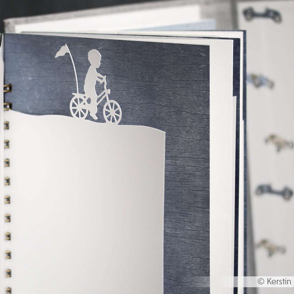 Ein weißer Papierausschnitt aus der Alexandra Renke Motivstanze Kind auf Fahrrad ziert eine spiralgebundene Notizbuchseite, ideal um Ihre Lieblings 200g Designpapiere zu präsentieren.