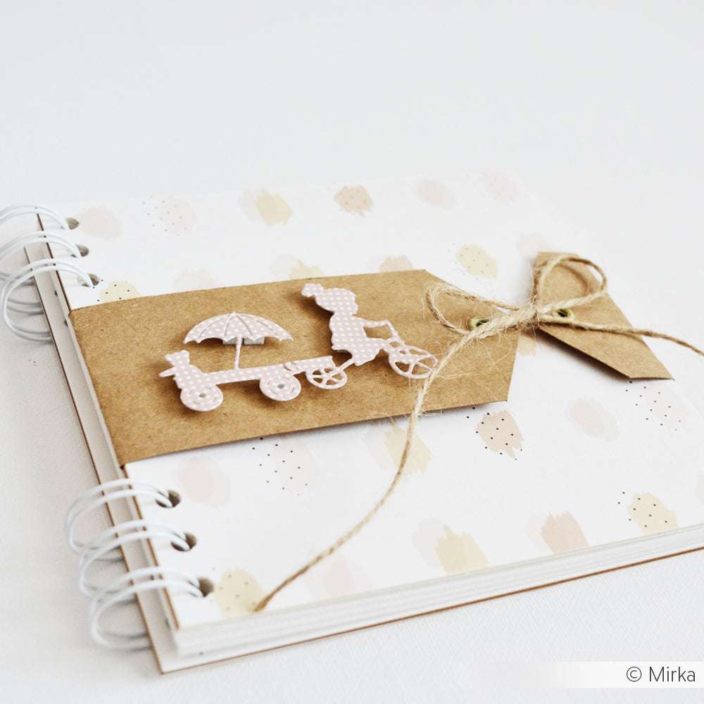 Ein spiralgebundenes Scrapbook von Alexandra Renke mit Kinderwagen-Dekoration, Rankenschleife und pastellfarben gepunktetem Einband, mit kreativen Akzenten aus Stanzen für Designpapiere.