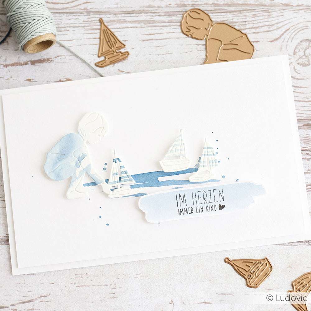 Grußkarte von Alexandra Renke mit einem Kind mit Papiersegelbooten und dem Text "IM HERZEN IMMER EIN KIND" auf Holz - gefertigt mit der Motivstanze Schiffsjunge für zusätzlichen Charme.