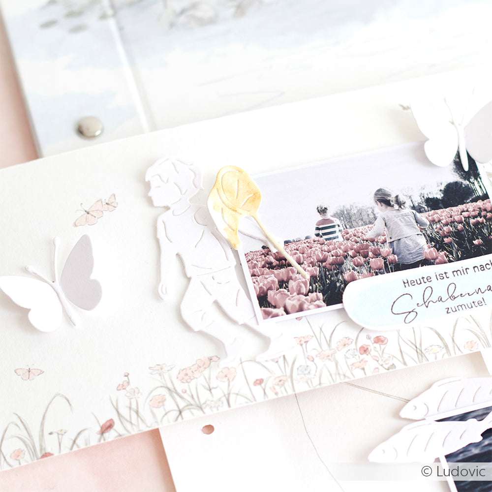 Scrapbook-Seite mit Papierausschnitten, Schmetterlingen, einem Kinderfoto in einem Tulpenfeld und zarten Akzenten, die mit Alexandra Renke Stanzen für Papier hergestellt wurden und für zusätzlichen Charme sorgen.