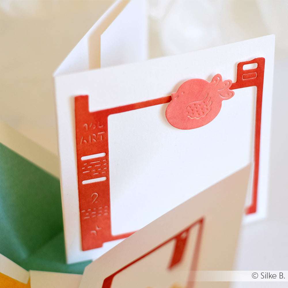 Weiße Grußkarte von Alexandra Renke mit roter Zierbordüre aus hochwertigen Designpapieren und einem rosa Granatapfel aus der Motivstanze Film Rahmen Stanzsysteme auf der Vorderseite.