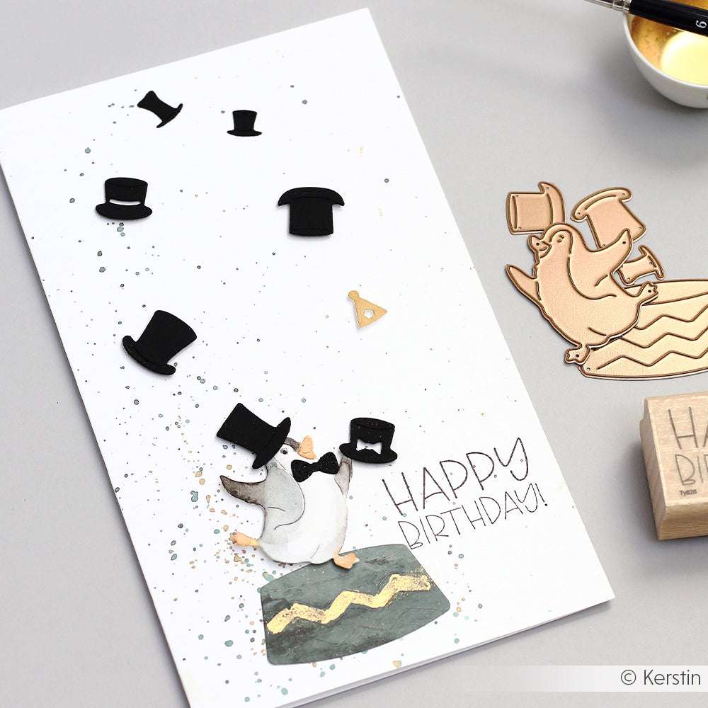 Handgemachte Geburtstagskarte von Alexandra Renke mit einem Pinguin, der schwarze Zylinder wirft, mit Motivstanze gestanzt und "HAPPY BIRTHDAY!" auf der Vorderseite.