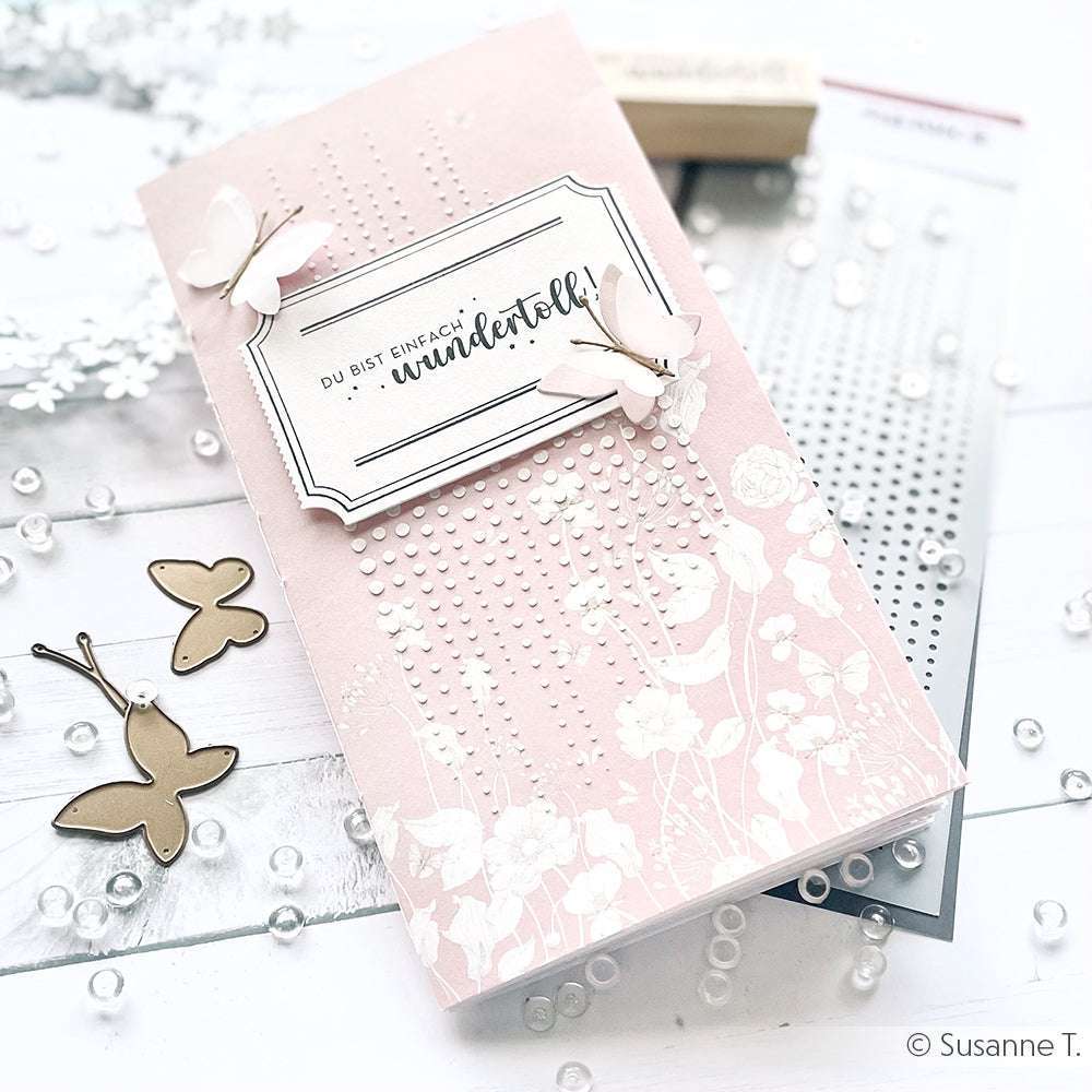 Rosa handgefertigte Karte von Alexandra Renke mit weißem Blumenmuster, Schmetterlingen aus dem Motivstanze Schichtschmetterling DieCut System, deutschem Text und umgeben von Designpapier, Bastelmaterial und Perlen.