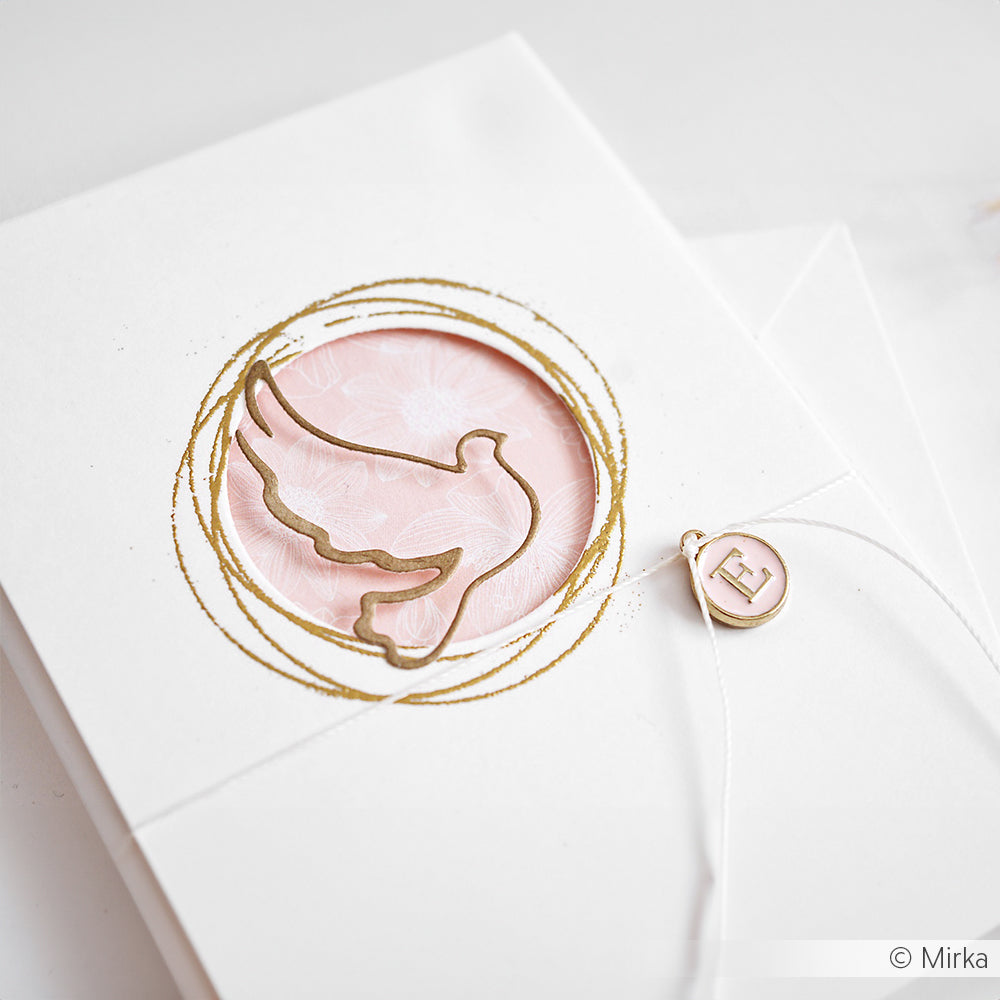 Weiße Karte von Alexandra Renke mit einer goldfarbenen Taube, die mit einer Motivstanze gestaltet wurde, einem rosa Hintergrund und einem runden Anhänger mit dem Buchstaben E an einer weißen Schnur.
