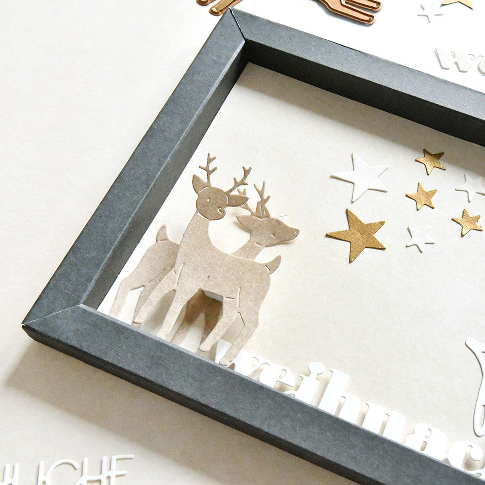 Rentiere aus Alexandra Renke Designpapieren, verziert mit goldenen Sternen, die mit den Motivstanze Tierische Sternfreunde Dies hergestellt wurden, und in einem Schattenbox-Rahmen vor einem hellen Hintergrund präsentiert.