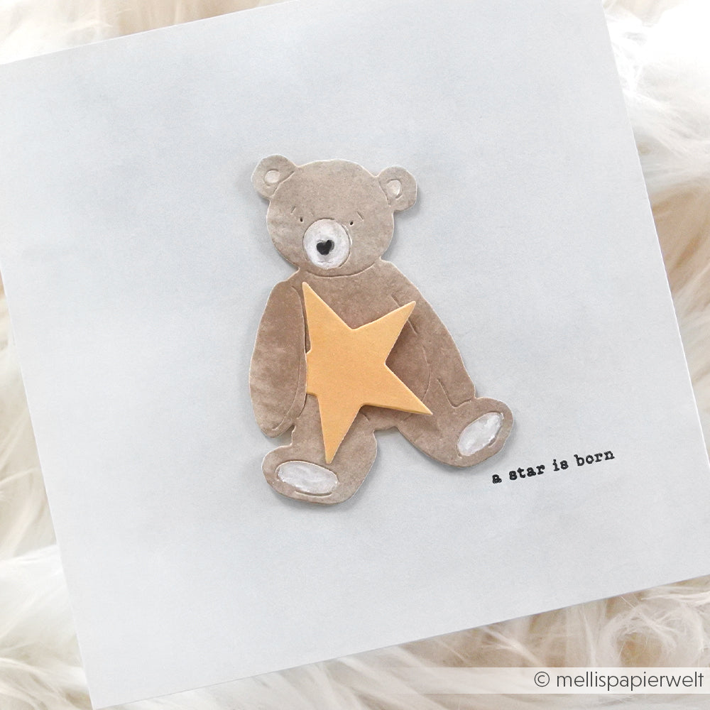 Ein brauner Teddybär hält einen gelben Stern mit der Aufschrift "a star is born" auf hellem Hintergrund - perfekt für Ihre Motivstanze oder DieCut Systeme beim Basteln von Karten und Designpapieren von Alexandra Renke.