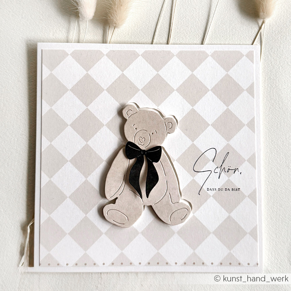 Grußkarte von Alexandra Renke mit einem grauen Teddybär mit schwarzer Schleife auf hellkariertem Hintergrund, gestaltet mit Motivstanze Bärchen und stilvollen Designpapieren, mit deutschem Text.