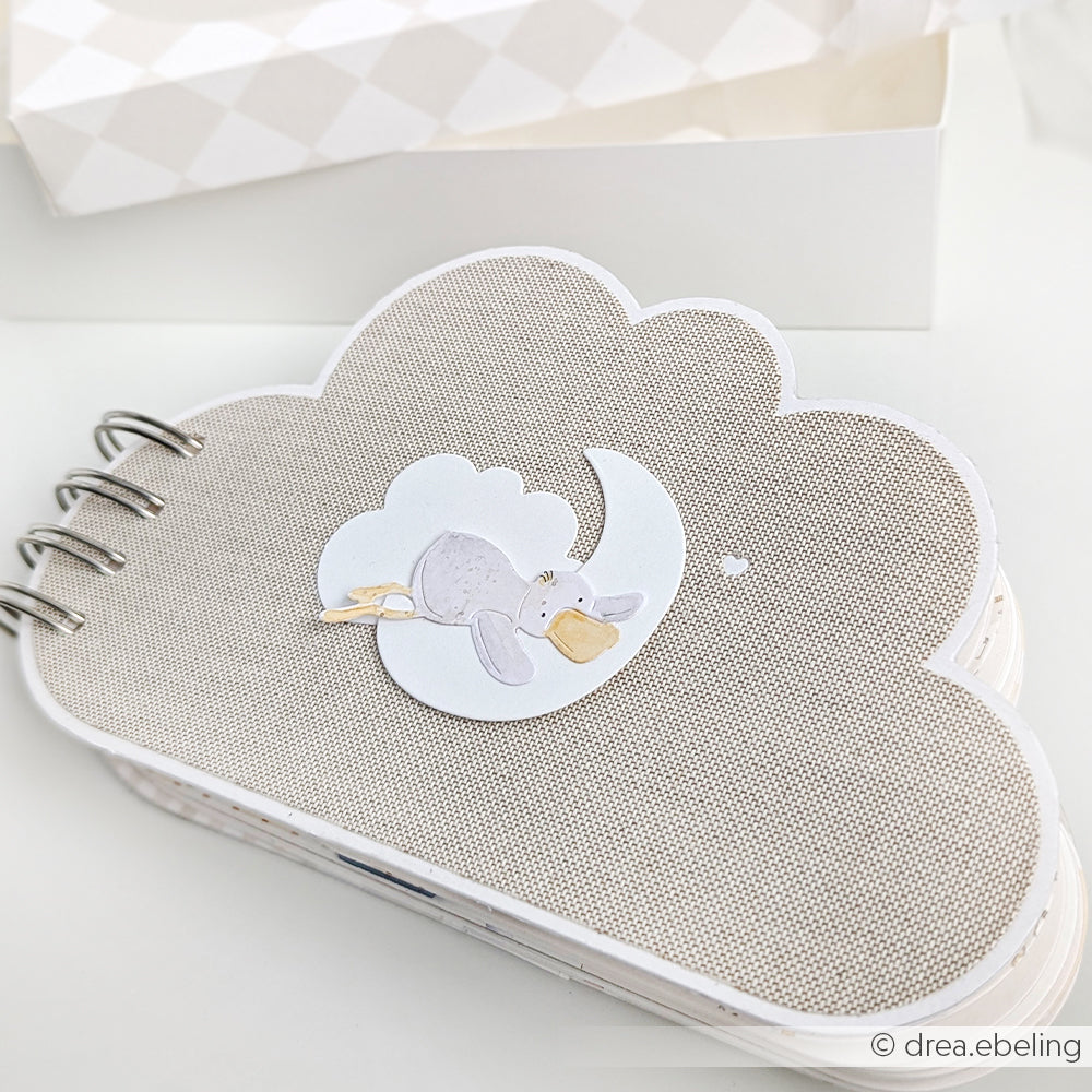 Das wolkenförmige Scrapbook von Alexandra Renke hat einen grauen, strukturierten Einband mit einem schlafenden Elefanten auf einem Mond, der mit Stanzsystemen hergestellt und mit charmanten Designpapieren verziert wurde.
