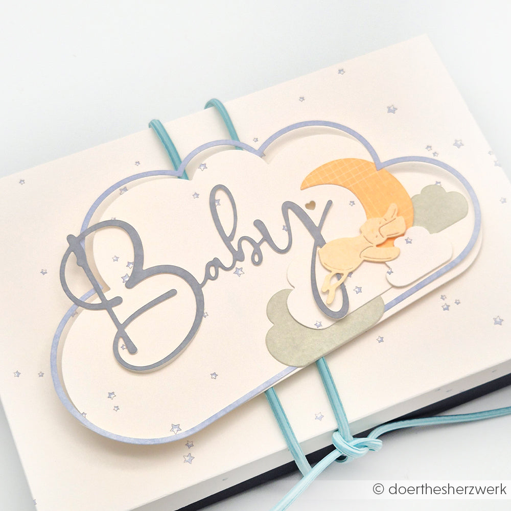 Die wolkenförmige Karte von Alexandra Renke zeigt den Text "Baby", Sterne, einen gelben Mond und einen schlafenden Hasen - ideal für die Verwendung mit Stanzen für Designpapiere oder DieCut Systeme, um bezaubernde handgemachte Babygeschenke zu basteln.