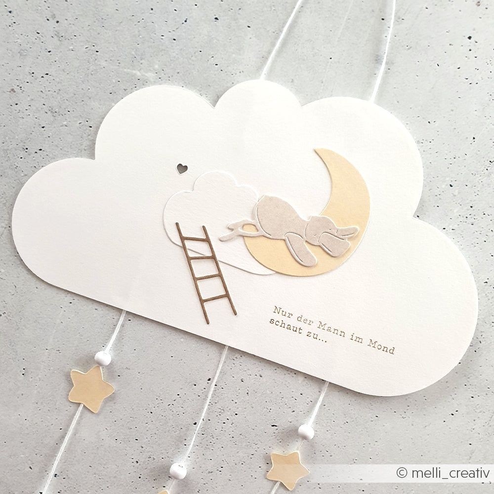 Die Papierkunst, die mit Alexandra Renke Stanzen hergestellt wurde, zeigt einen Hund, der auf einem Mond schläft, Wolken, hängende Sterne und eine Leiter - perfekt für Projekte mit Stanzen für Designpapier auf grauem Hintergrund.