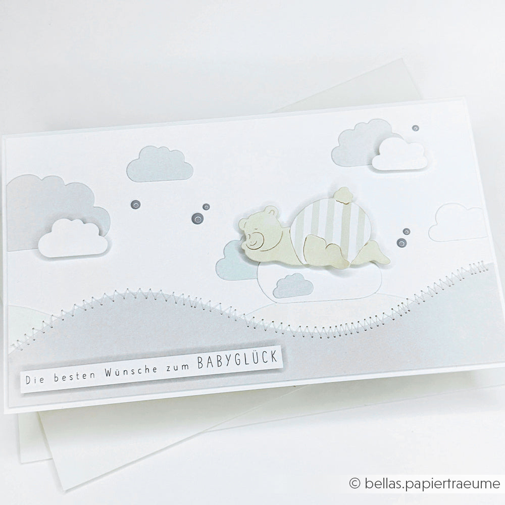Eine niedliche, neutral getönte Karte von Alexandra Renke mit einem Bären auf Wolken und einem deutschen Text, der dem Baby Glück wünscht, wurde mit Designpapieren und Motivstanze Schlafgefährten gestaltet.