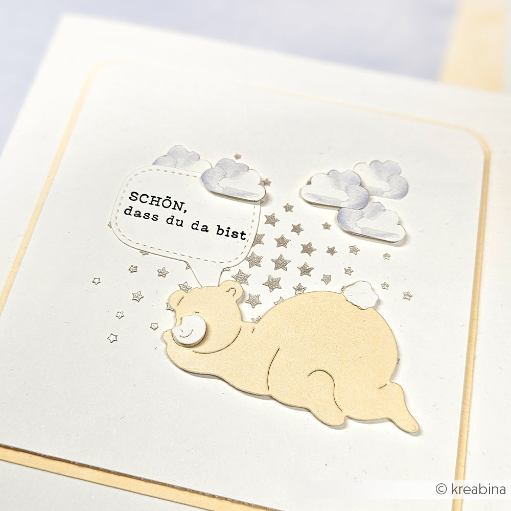 Eine niedliche Bärenillustration von Alexandra Renke Motivstanze Schlafgefährten mit Wolken, Sternen und einer Sprechblase mit dem Spruch SCHÖN, dass du da bist.