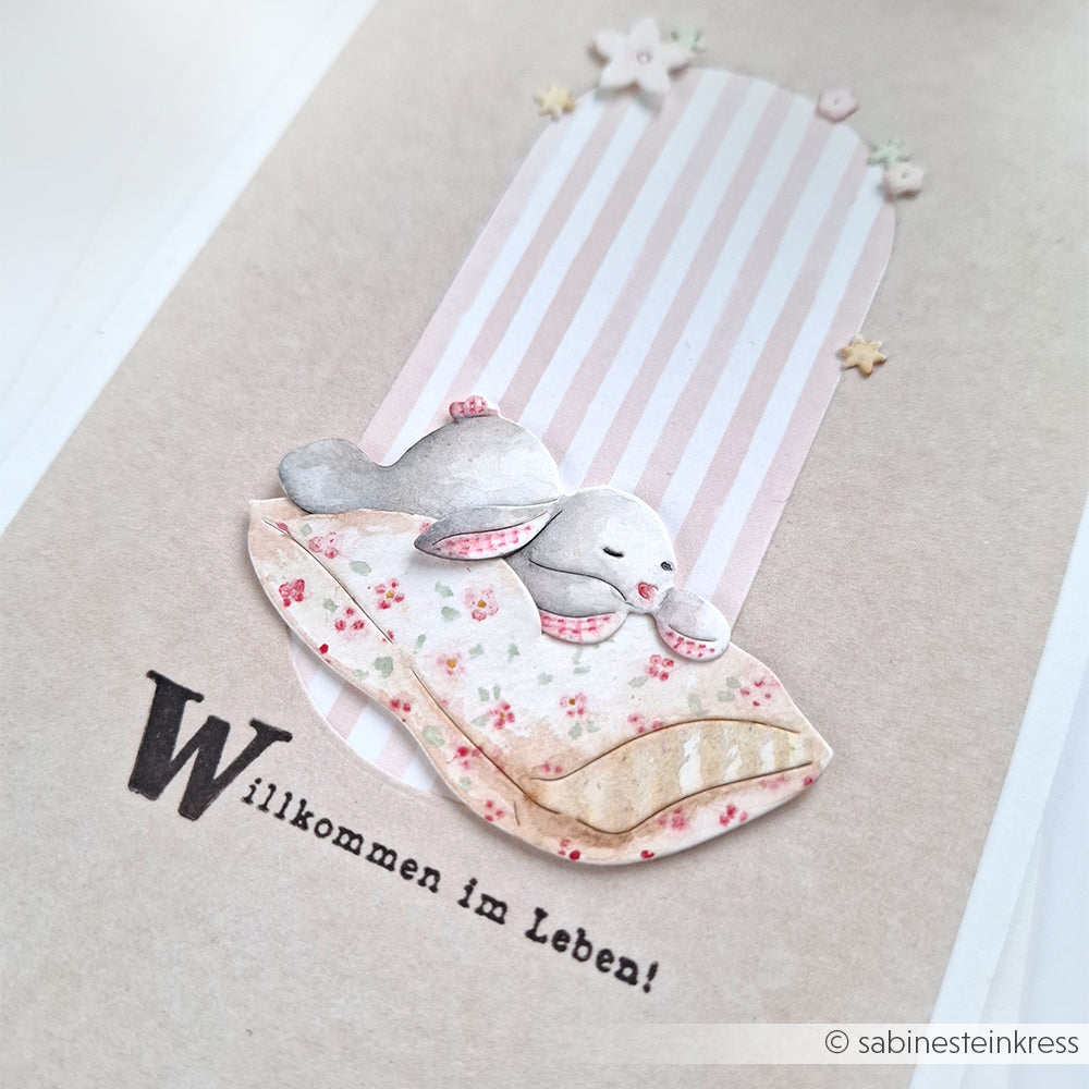 Alexandra Renke Grußkarte mit einem niedlichen Hasen auf einem Kissen, gestreiftem Hintergrund und dem Text "Willkommen im Leben!" - ideal für die Verwendung mit Stanzen für Designpapier oder Ihren bevorzugten DieCut Systemen.