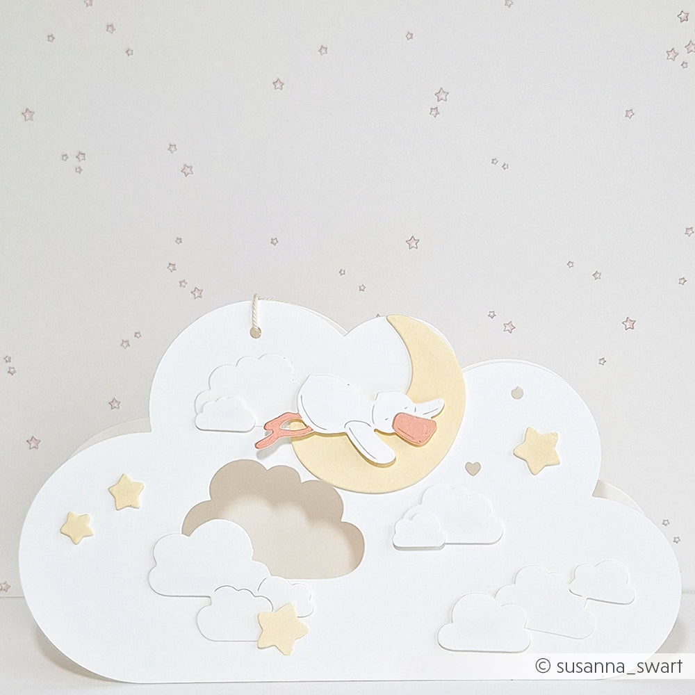 Ein Storch schläft auf einer Mondsichel, umgeben von Wolken und Sternen vor einem blassen, sternenklaren Hintergrund, der den zarten Charme der Designs von Alexandra Renke widerspiegelt.