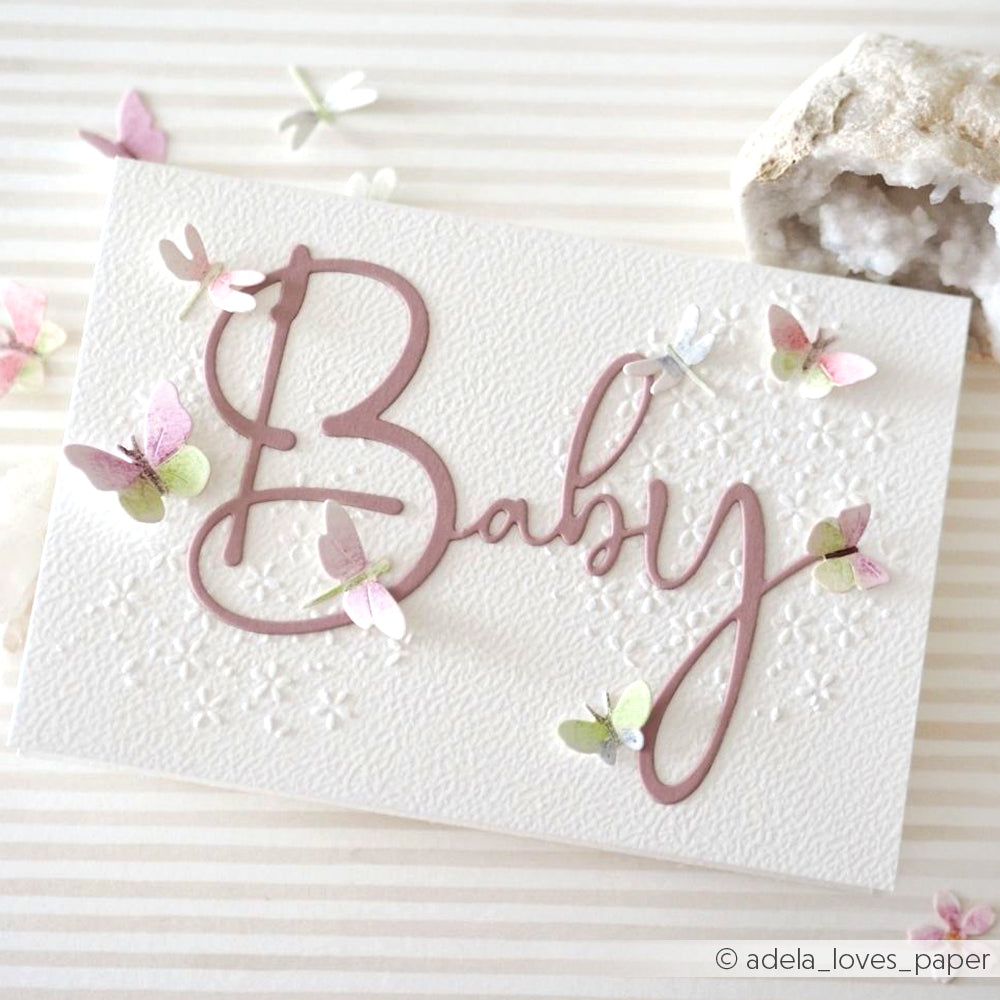 Handgefertigte Karte von Alexandra Renke mit dem Schriftzug "Baby" und gestanzten Schmetterlingen aus pastellfarbenem Designpapier auf einem strukturierten weißen Hintergrund.