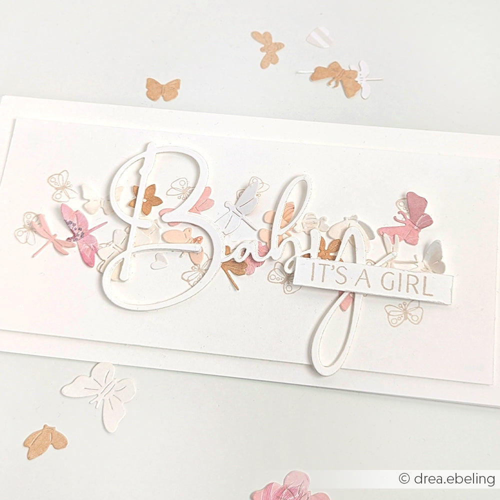 Die handgefertigte Karte von Alexandra Renke zeigt pastellfarbene Schmetterlinge, die mit Designpapieren und Motivstanze hergestellt wurden, und ist mit den Worten "Baby" und "IT'S A GIRL" in dekorativer Schrift verziert.