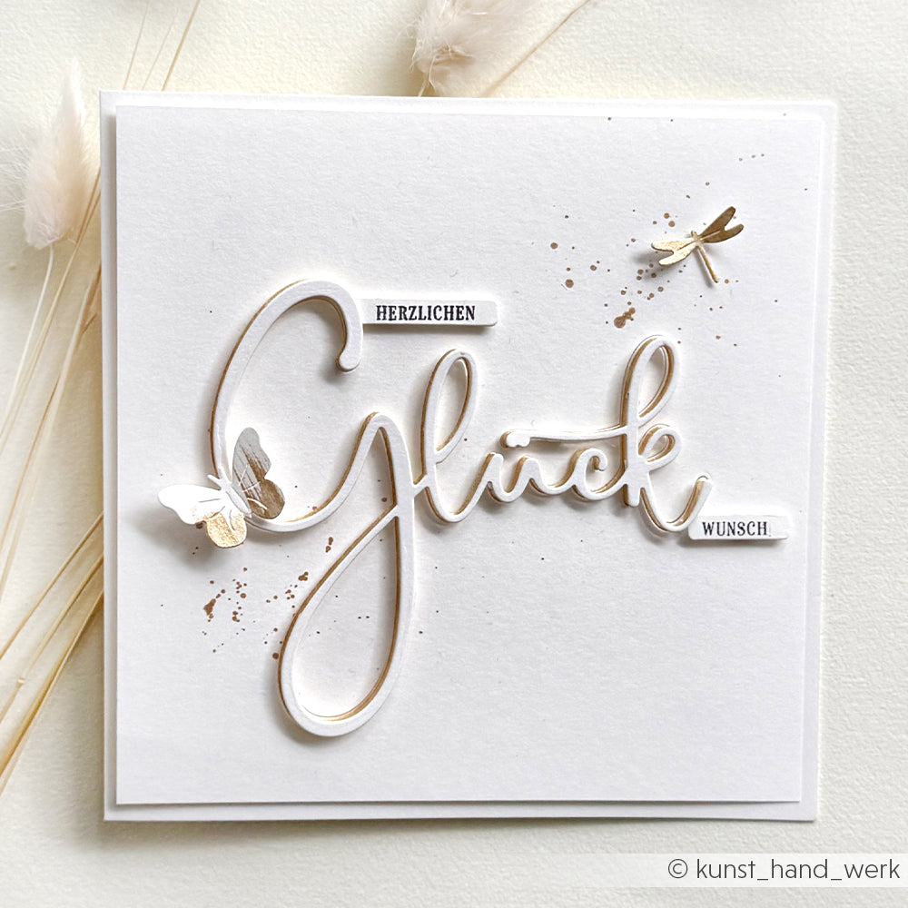 Quadratische Karte von Alexandra Renke mit "Glück"-Schriftzug, goldenen Schmetterlingen, Libelle und "Herzlichen Wunsch" auf Weiß - ideal zu Motivstanze oder Ihren Lieblingsdesignpapieren.
