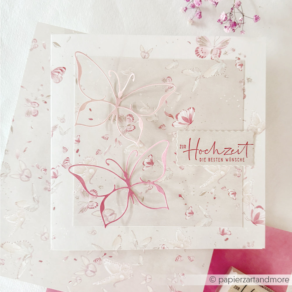 Die quadratische Karte von Alexandra Renke mit rosa Schmetterlingen, gestaltet mit Designpapieren und der Motivstanze „Schmetterling“, zeigt den deutschen Text „Zur Hochzeit die besten Wünsche“ auf einem blumigen Hintergrund.