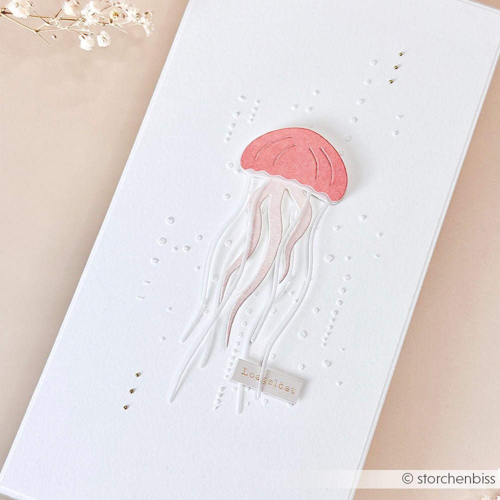 Minimalistische Karte mit einer rosa Qualle, die mit der Stanzform „Qualle“ aus der Motivstanze-Serie von Alexandra Renke gestaltet wurde, sowie geprägten Punkten auf strahlend weißem Hintergrund, akzentuiert durch Trockenblumen in der Ecke – perfekt als Ergänzung zu Ihrer Sammlung einzigartiger Designpapiere von Alexandra Renke.