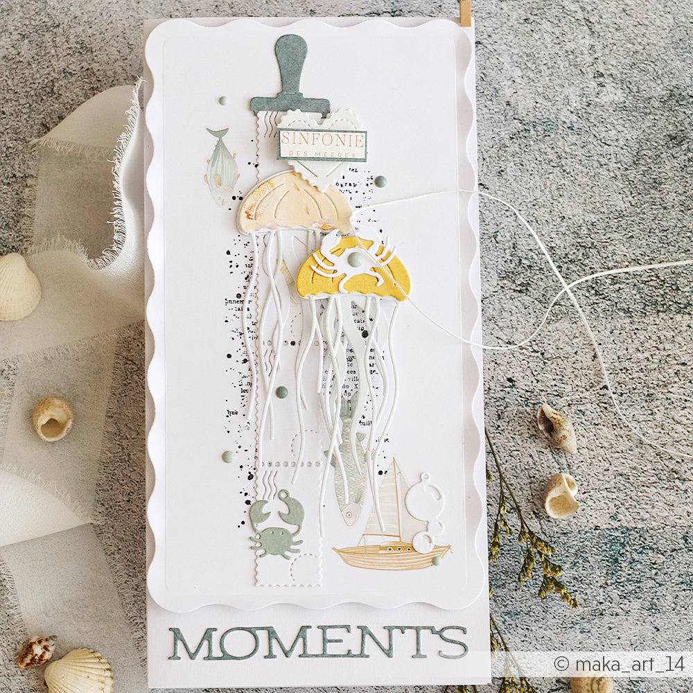 Handgefertigte Karte mit Quallen- und Meeresmotiven, Muscheln und dem Schriftzug „MOMENTS“ am unteren Rand auf einer strukturierten Oberfläche, gestaltet mit den Stanzformen „Motivstanze Qualle“ von Alexandra Renke und eleganten Designpapieren von Alexandra Renke.