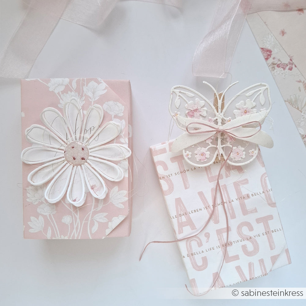 Zwei pastellrosa Geschenkboxen von Alexandra Renke, gefertigt aus elegantem Designpapier, sind mit einer Blumen- und Schmetterlingsverzierung versehen, die mit dem Stanzsystem „Blumiger Schmetterling“ von Motivstanze gestaltet wurde.