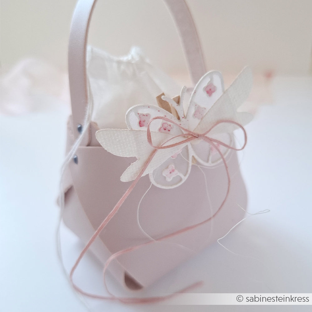 Hellrosa Geschenktüte von Alexandra Renke mit einem zarten „Motivstanze Schmetterling“-Motiv und einer Schleife, gefertigt aus edlen Designpapieren auf einem sanften weißen Hintergrund.