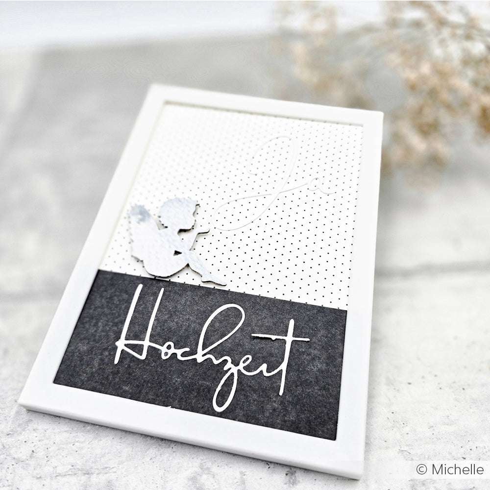 Weiße Karte von Alexandra Renke mit Cherub-Silhouette und Schriftzug "Hochzeit", erstellt mit der Motivstanze Hochzeit auf gepunktetem Designpapier, vor dunklem Hintergrund.