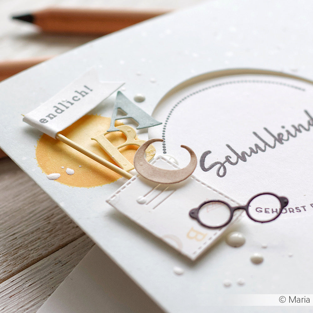 Alexandra Renke Grußkarte mit deutschem Text, hergestellt mit Motivstanze Gemischtes Alphabet und Designpapieren, mit ausgeschnittenen Buchstaben, einer Brille, einer Flagge und einer Mondsichel.