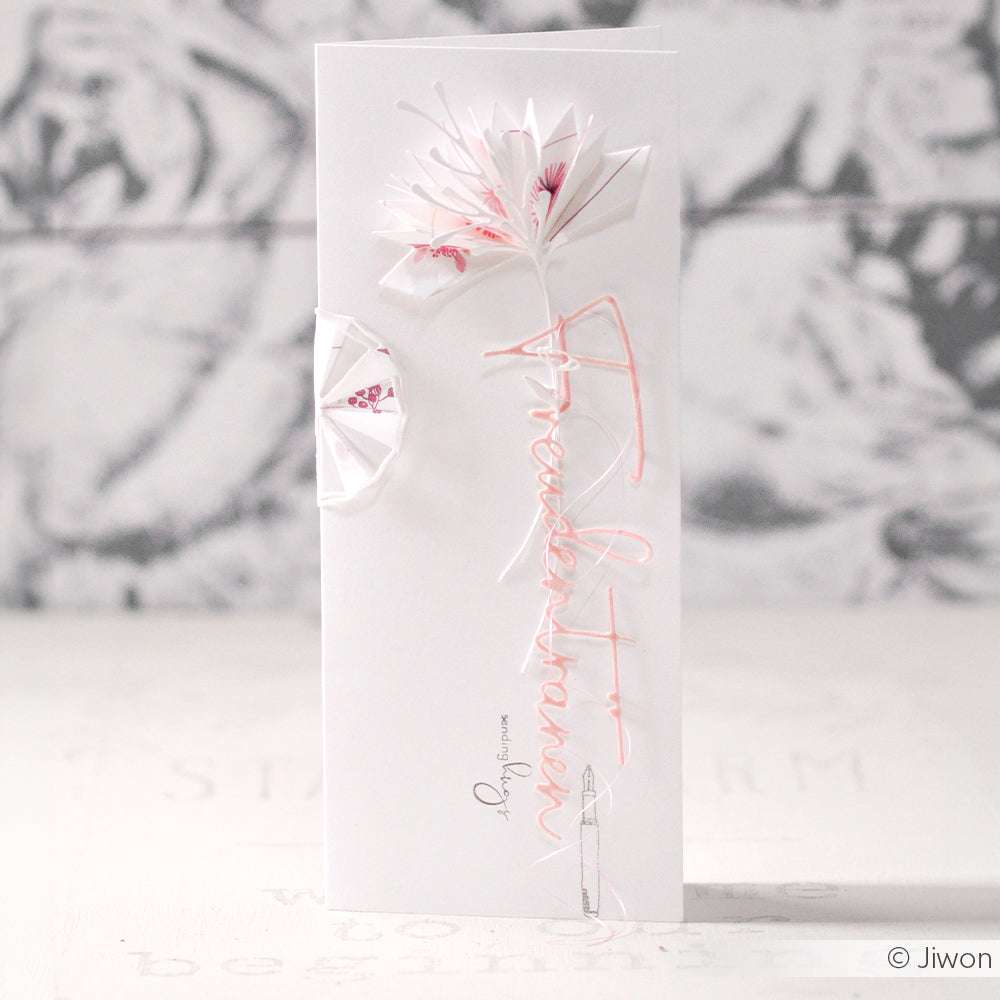 Eine zarte weiße Karte von Alexandra Renke mit einer Origamiblume und einem kursiven "Glückwunsch" in Rosa - perfekt, um sie mit Stanzschablonen oder Dies für Basteln zu kombinieren und ihr eine handgemachte Note zu verleihen.