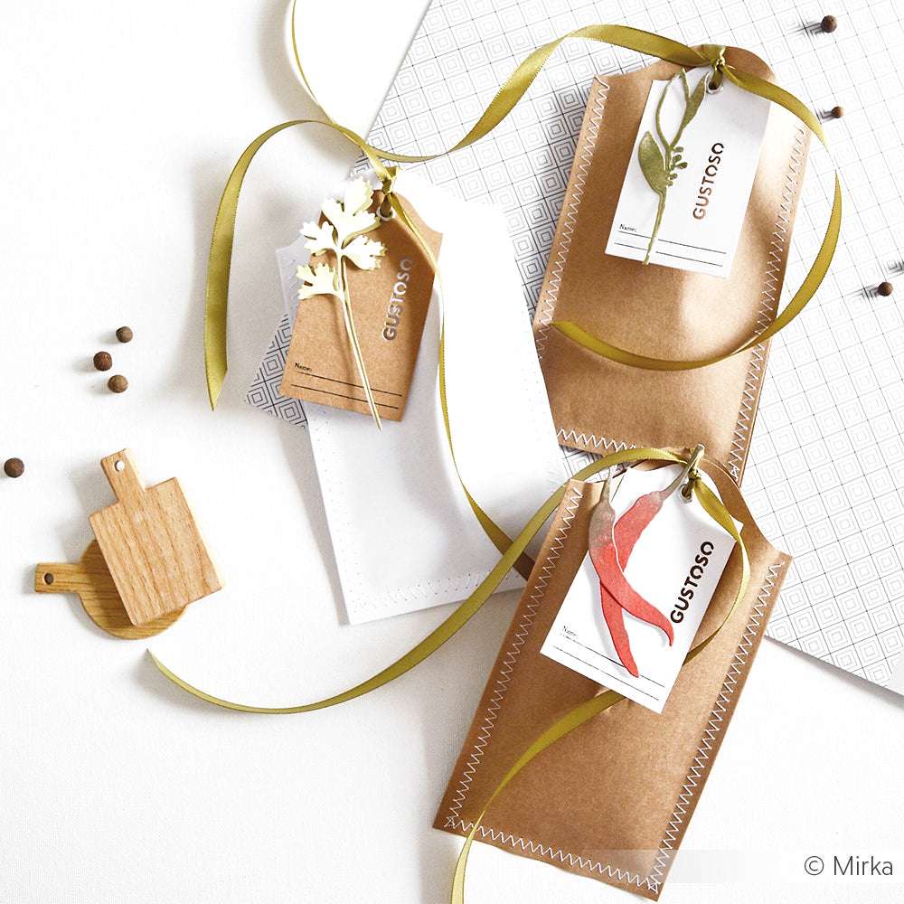 Alexandra Renke Geschenktüten mit Schleife, Anhängern und einem hölzernen Dreidel werden auf einem weißen Hintergrund mit verstreuten Pfefferkörnern präsentiert - ideal zum Kombinieren mit Stanzformen oder Motivstanze aus Ihrem bevorzugten Stanzsystem für individuelle Veredelungen.